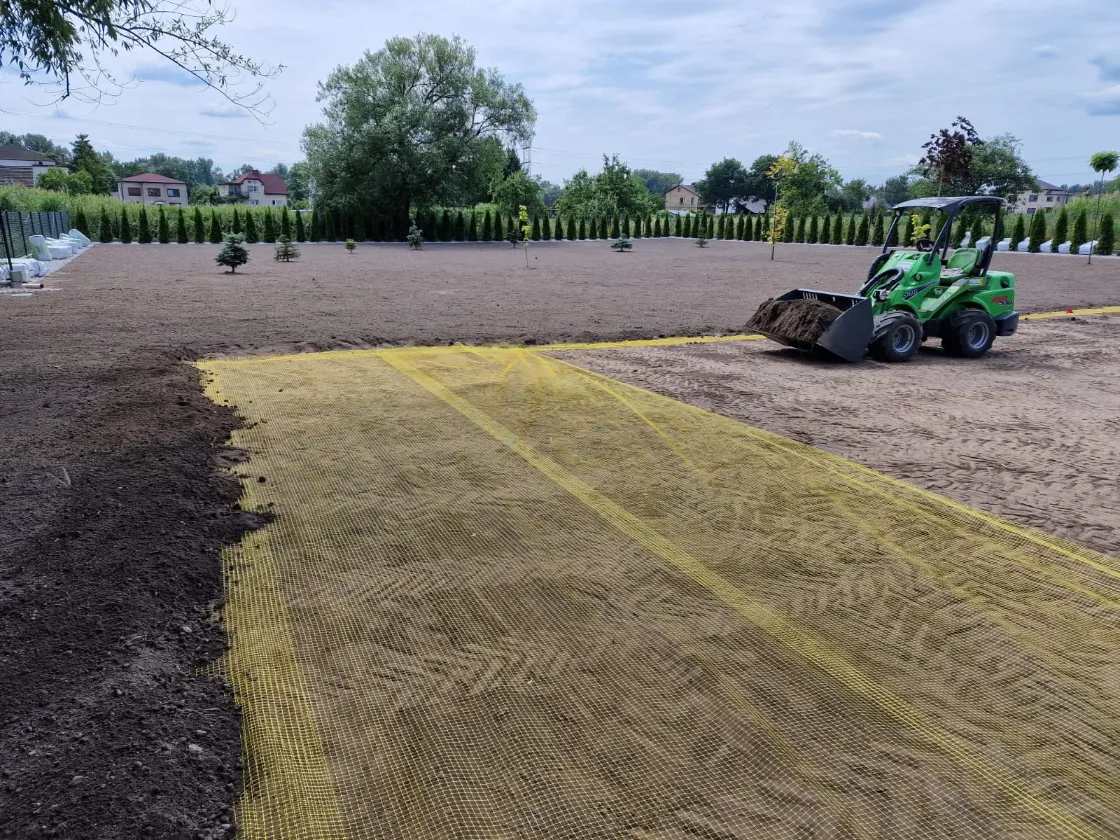 Ładowarka rozwozi ziemię po wyrównanym terenie z siatką na krety