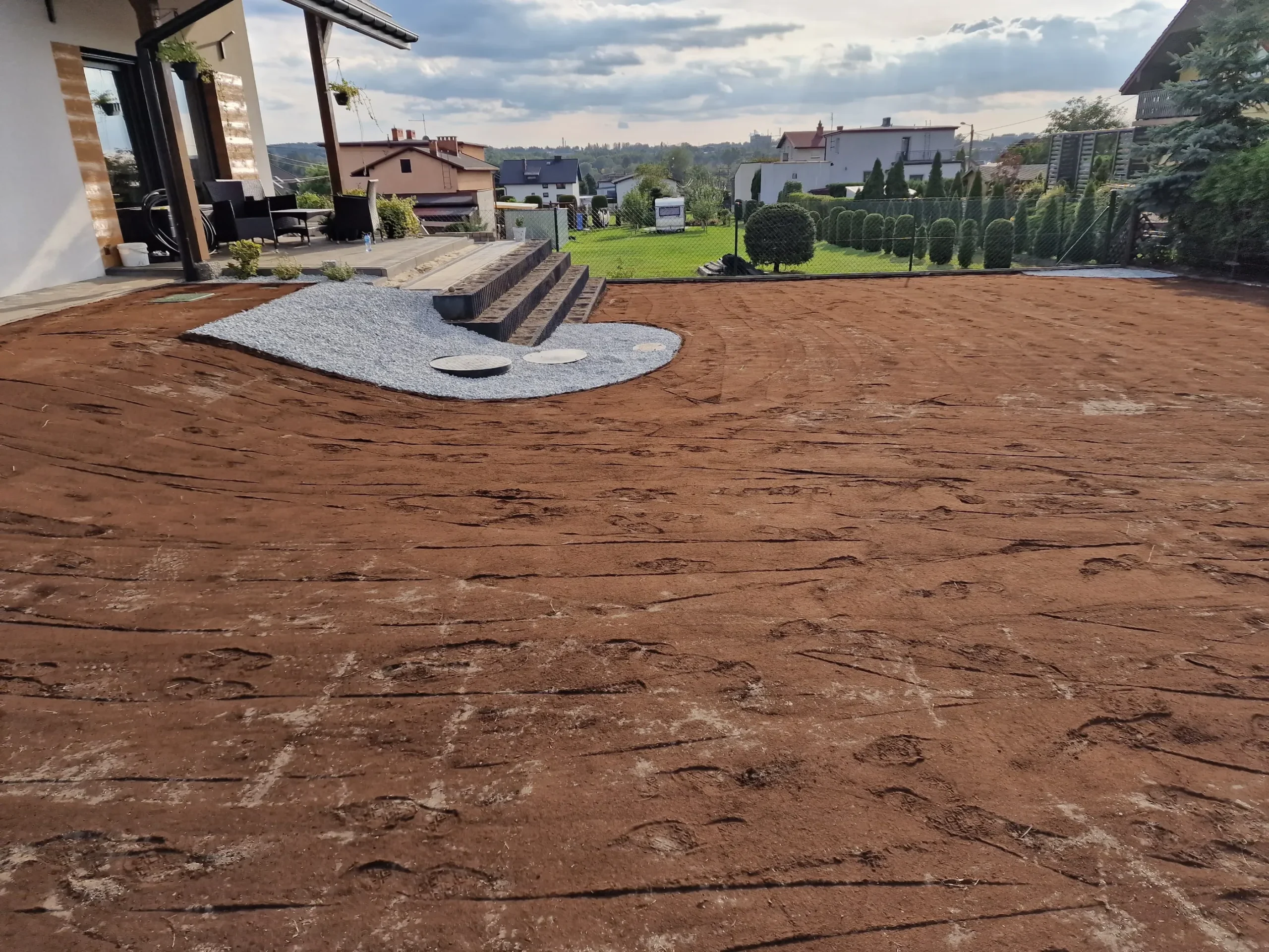 Przygotowanie terenu z wyrównaną ziemią przed tarasem pod trawnik