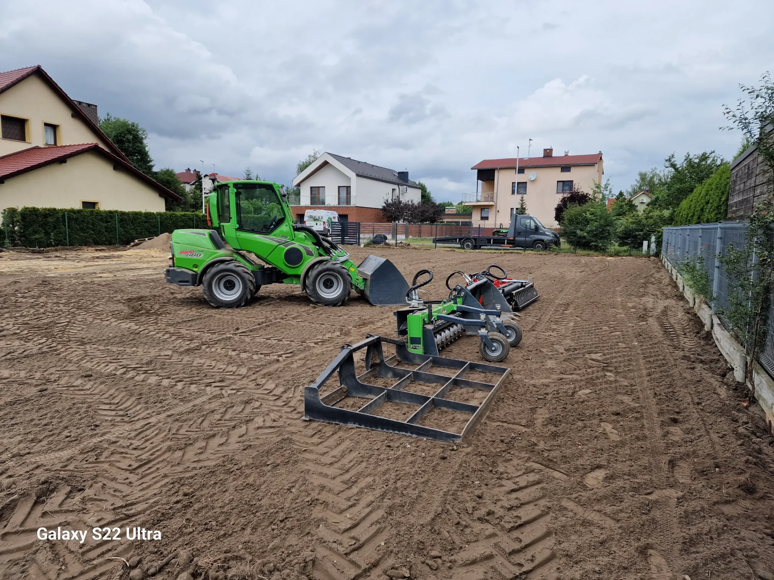 Ładowarka z osprzętem na wyrównanym gruncie przed domami, niwelacja terenu