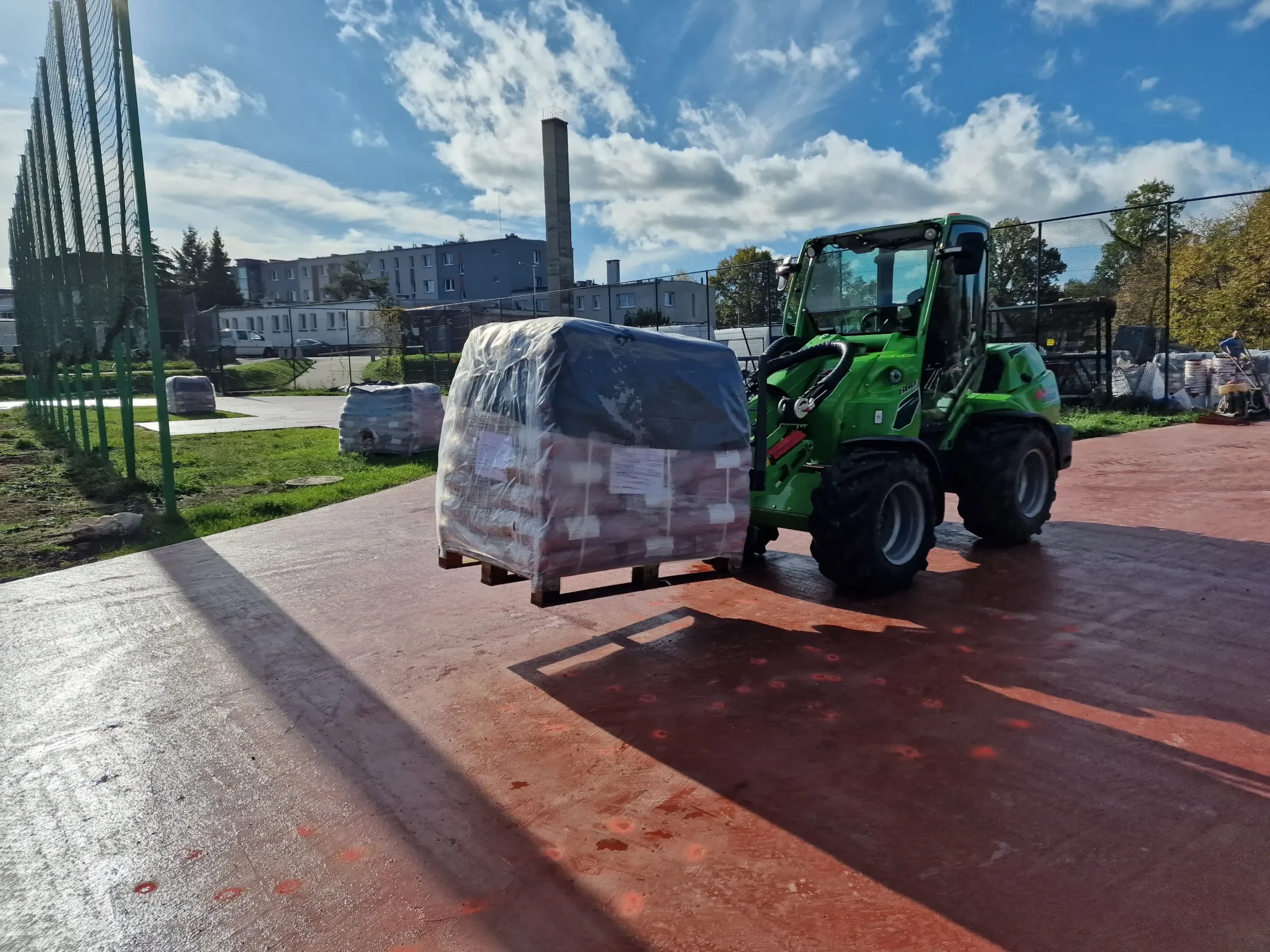 Usługi ładowarką: zielona ładowarka przenosi paletę materiału na przygotowanym podłożu