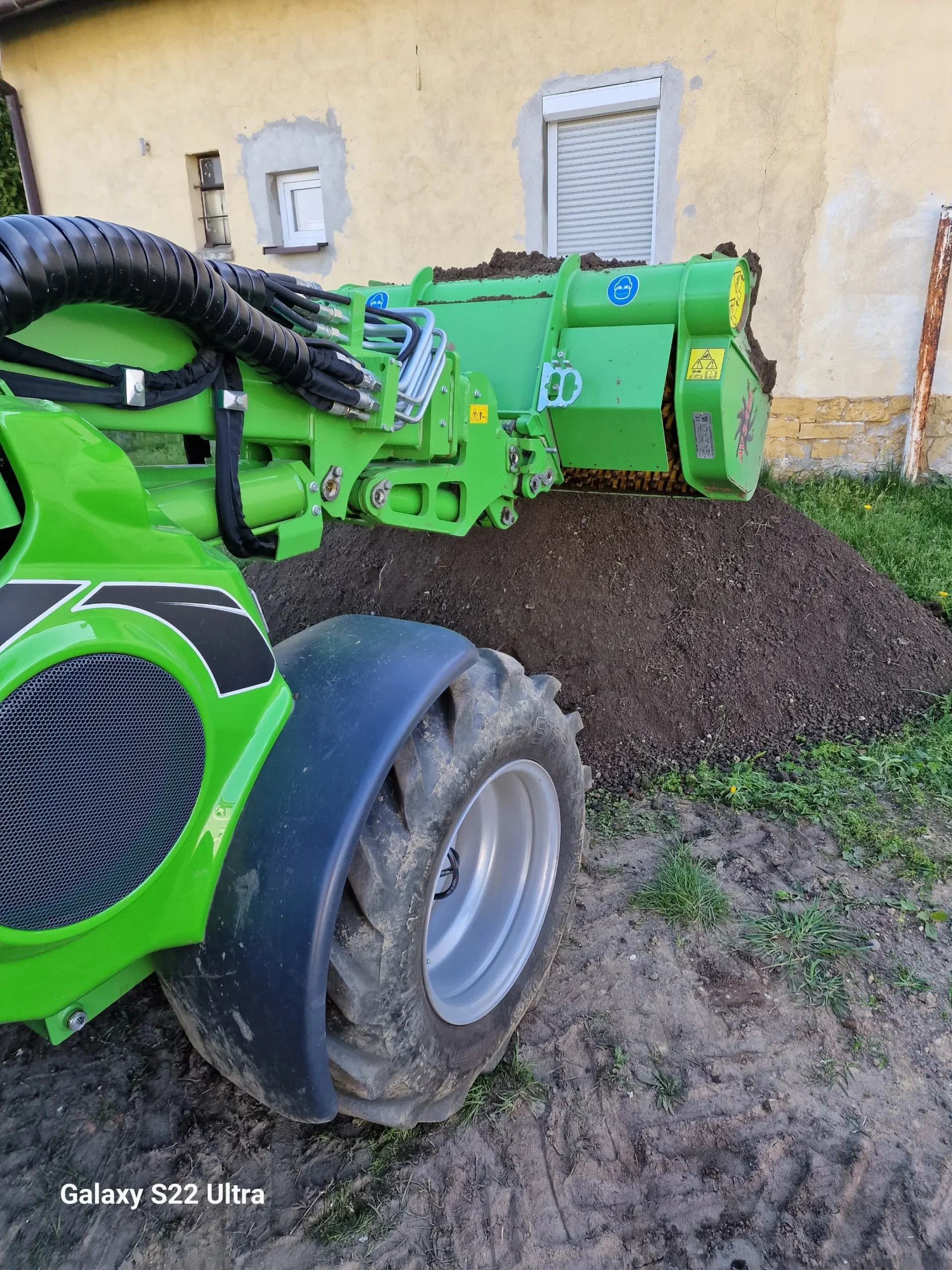 Przesiewanie ziemi przy budynku za pomocą zielonej ładowarki z przesiewaczem oddzielającej ziemię