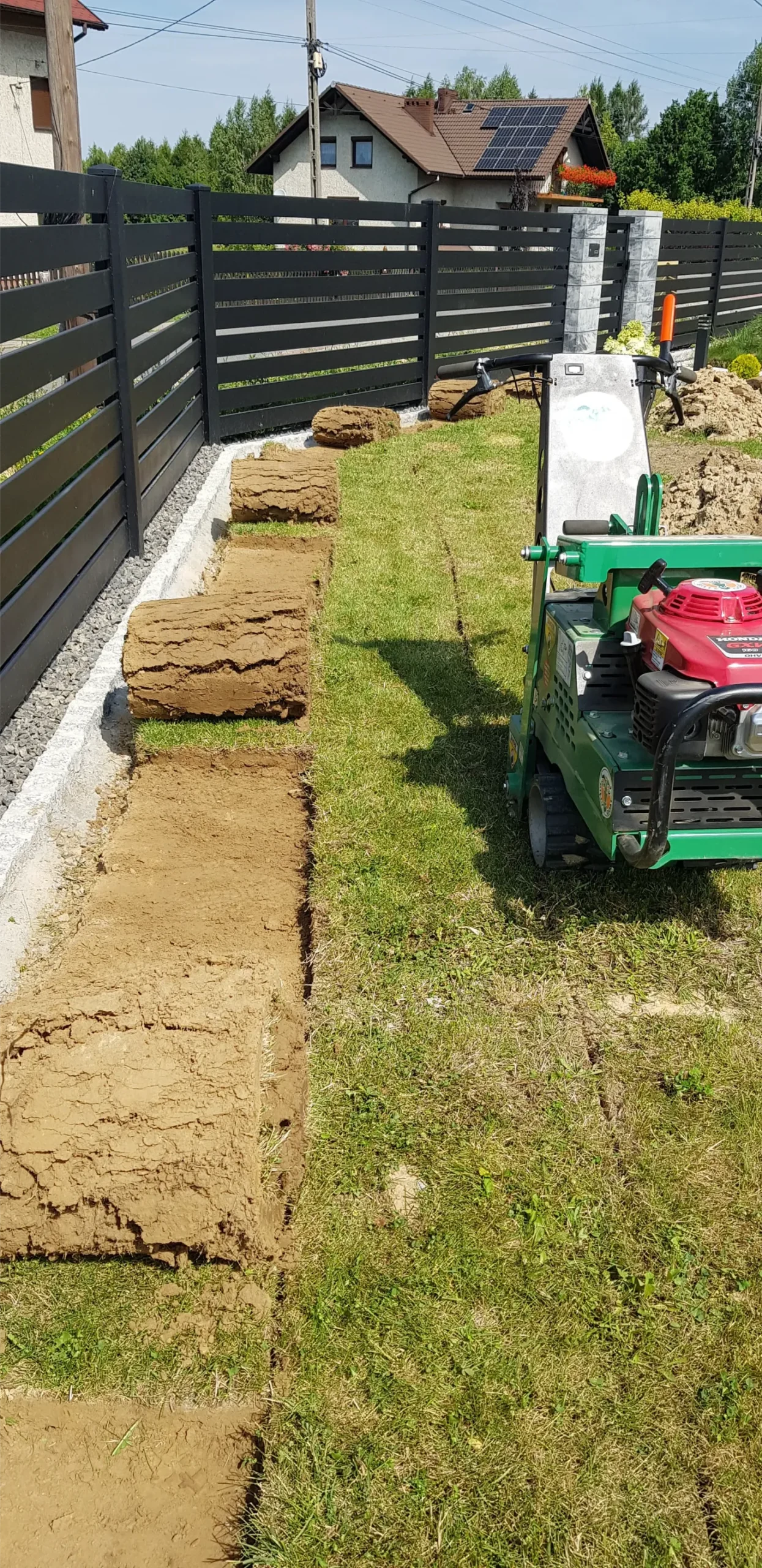 Wycięcie darniny – maszyna do cięcia trawy wycina pasy darni obok czarnego ogrodzenia