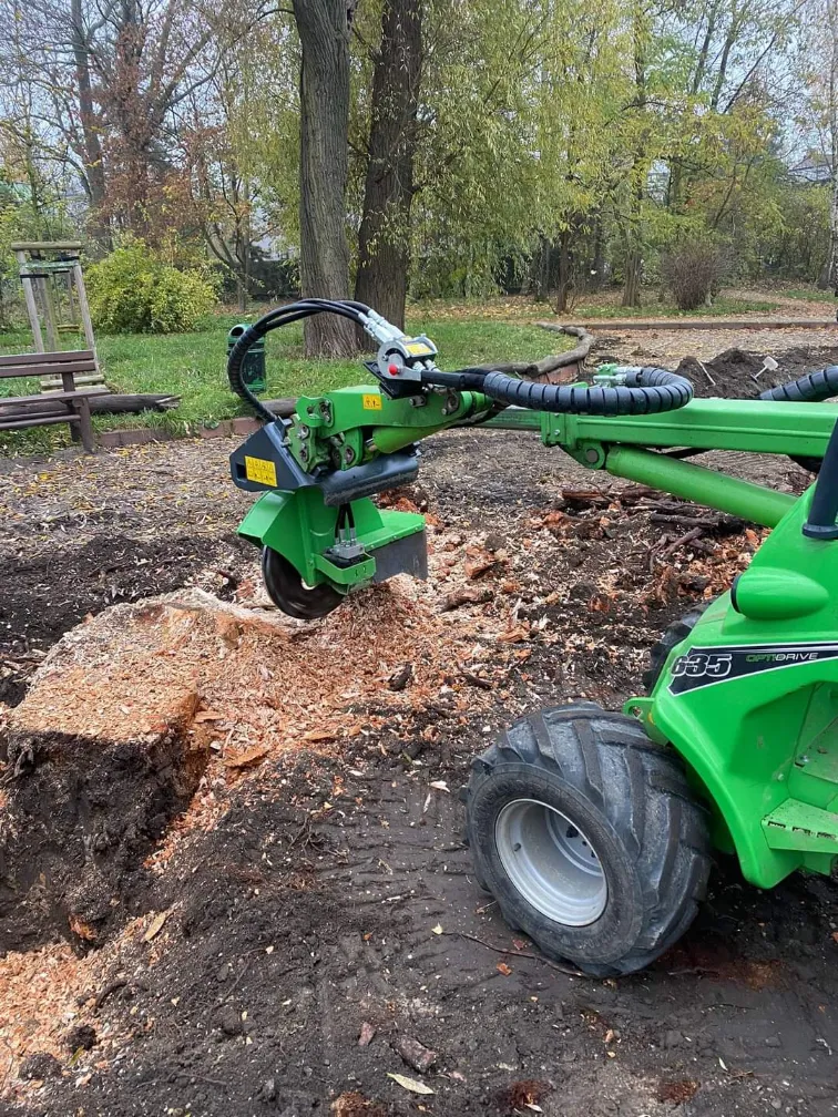 Frezowanie pni minikoparką – zielona maszyna z frezem obrabia pień drzewa, widoczne zrębki drewna