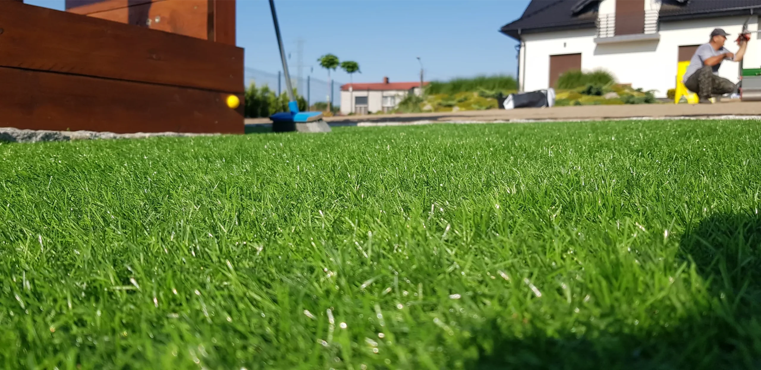 Trawa z rolki na przedogródku – równy świeżo położony zielony dywan z rolki z widocznym pracownikiem w tle