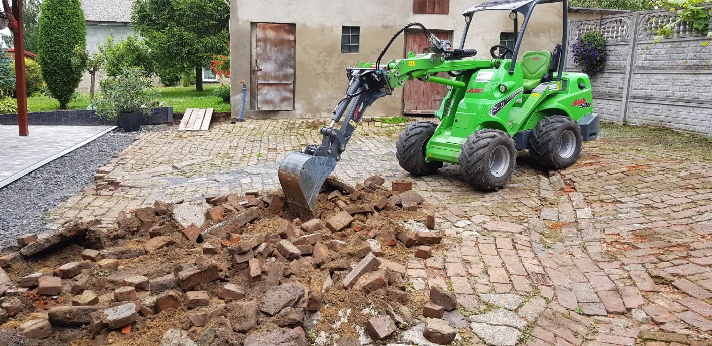 Usługi minikoparką zieloną maszyną rozbiórka starej kostki brukowej i przygotowanie podłoża pod nowy podjazd