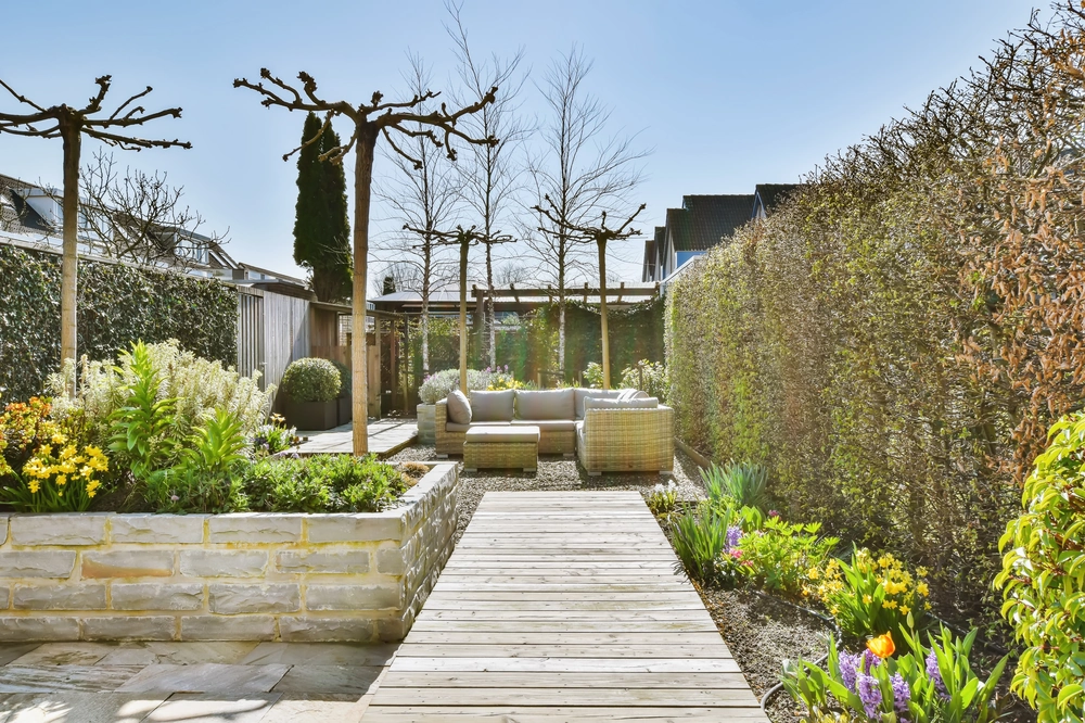 Aranżacja ogrodów z drewnianą ścieżką, podwyższonymi rabatami i wygodnym narożnikiem wypoczynkowym